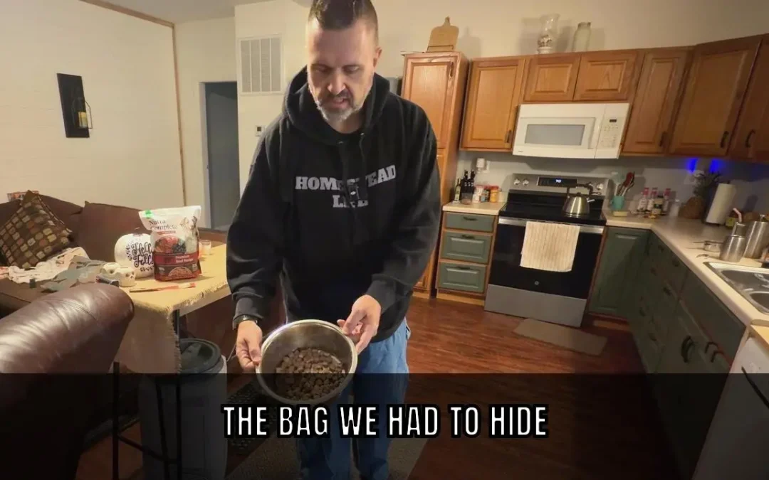 Ryan Harden in a homestead kitchen holds a metal bowl of Nutra Complete freeze-dried raw beef cubes, with the bag on the table behind him. Overlay text reads: The bag we had to hide.
